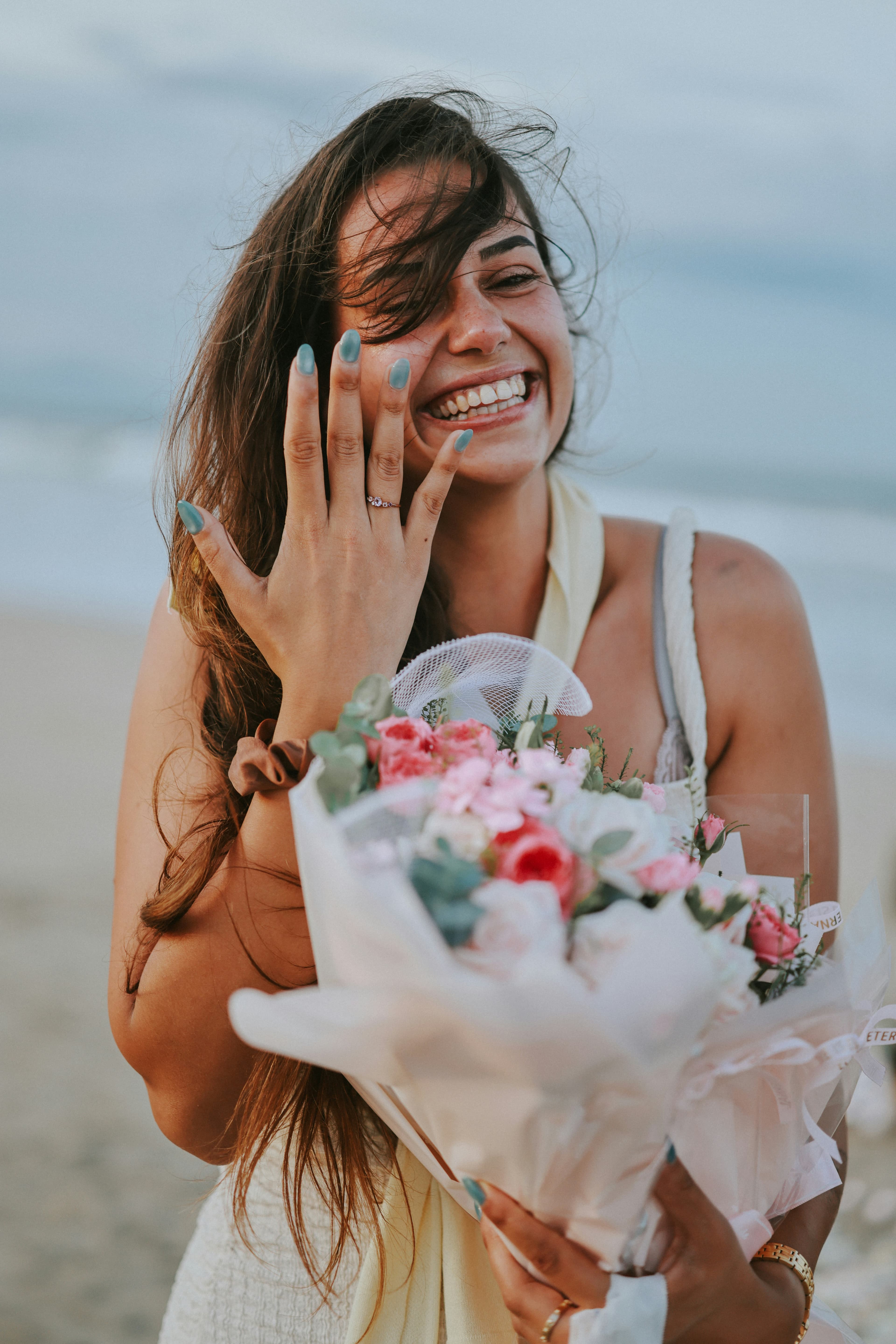 Woman showing her engagement ring, laughing on the beach